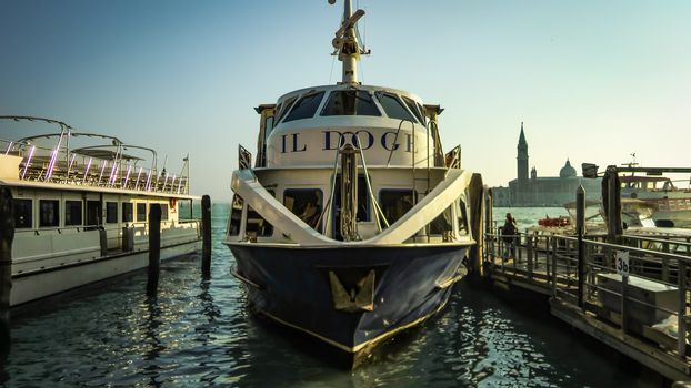 View of a part of the Venetian lagoon with a typical ferry docked on the pier at sunset.