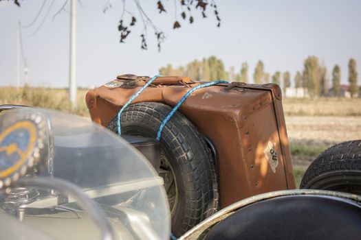 Old vintage leather suitcase, attached to an old vintage vehicle Italian ready to go and venture into a new journey. Abientazione: Italian countryside.