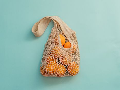 Mesh bag with fruits on blue background. Modern reusable shopping and zero waste concept.