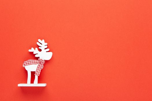 Christmas decoration, toy white deer in checkered scarf on red background with copy space. Festive, New Year concept. Horizontal, flat lay. Minimal style. Top view.