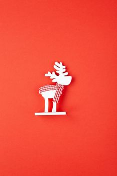 Christmas decoration, toy white deer in checkered scarf on red background. Festive, New Year concept. Vertical, flat lay. Minimal style. Top view.