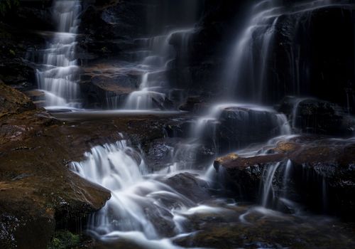 Cascading mountain stream flowing over rocks and cliff ledges as it meanders down into the valley