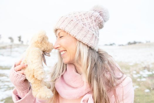 Smiling woman nose to nose with teddy bear outdoors in fresh snow
