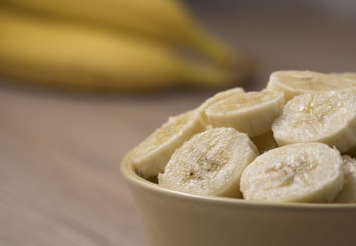 Fresh ripe organic sliced bananas in a ceramic bowl on a wooden table.
