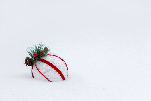 Red and white ball on a snowy Christmas tree.