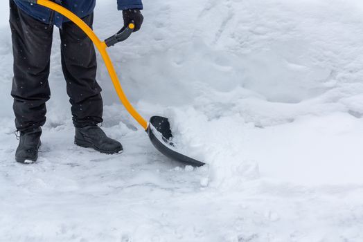 A man cleans snow in the yard with a shovel after a heavy snowfall.