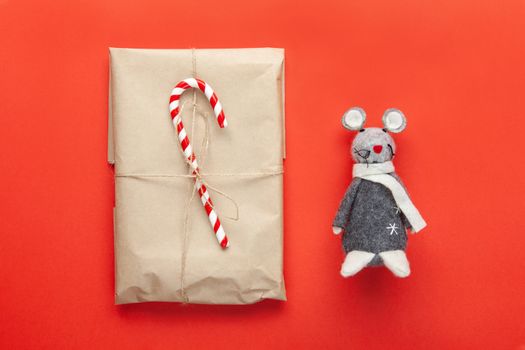 Grey toy rat, symbol of 2020 on Chinese calendar and Christmas gift wrapped in craft paper, decorated with cane candy on red background. Minimal style. Flat lay. Top view. Do it yourself concept.