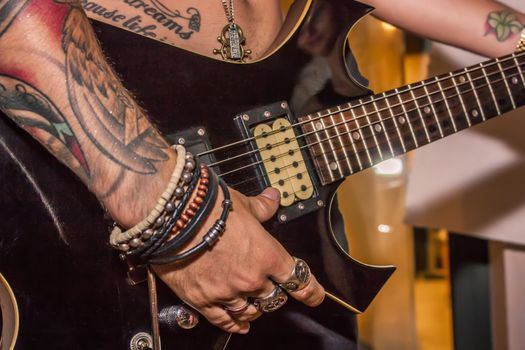 Detail of a tattooed boy playing electric guitar during a rock cone.