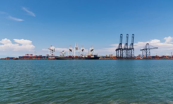 Cranes loading containers on large port cargo transport ship at day time