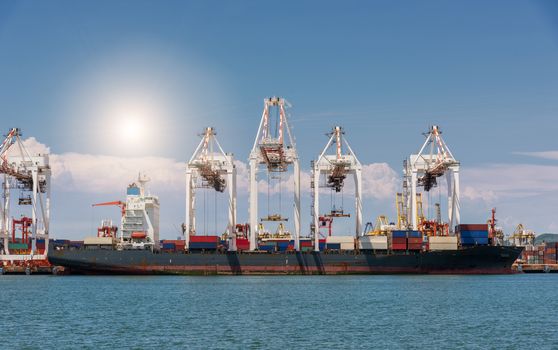 Cranes loading containers on large port cargo transport ship at day time