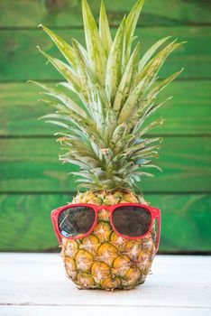 Holiday pineapple have sunglasses on green wooden background, tropical holiday concept