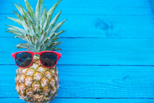 Holiday pineapple have sunglasses on blue    wooden background, tropical holiday concept