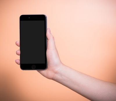 Female holding mobile smartphone plus blank screen on orange color background