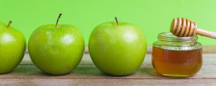 Jewish holiday, Apple Rosh Hashanah, on the photo have honey in jar and green apples on wooden with green background