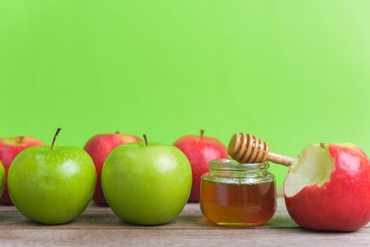 Jewish holiday, Apple Rosh Hashanah dessert, on the photo have honey in jar have red apples and green apples on wooden with green background