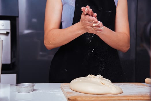 Hands of baker woman female making sprinkling clapping flour dough on table