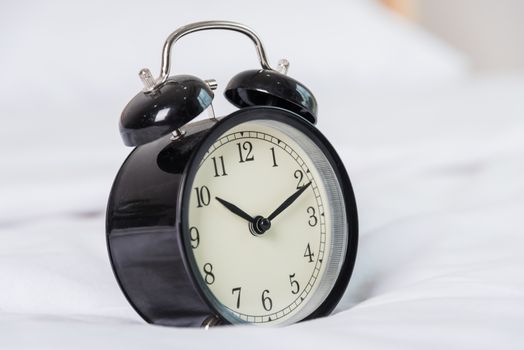 Black Alarm clock at 8 am on the bed. to wake up
