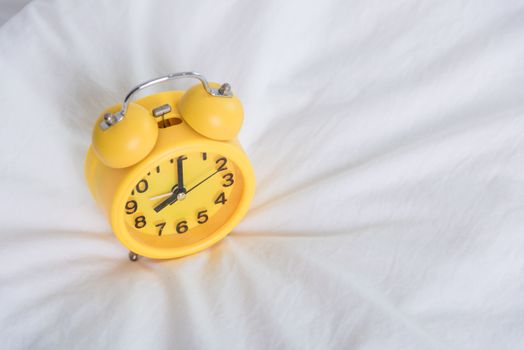 Yellow Alarm clock at 8 am on the bed. to wake up