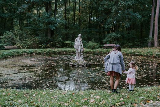 Beautiful little looking at the statue in the pond. Sunny day. Autumn day