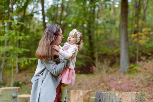 Mother holds daughter in her arms in the park on a sunny day. Autumn day