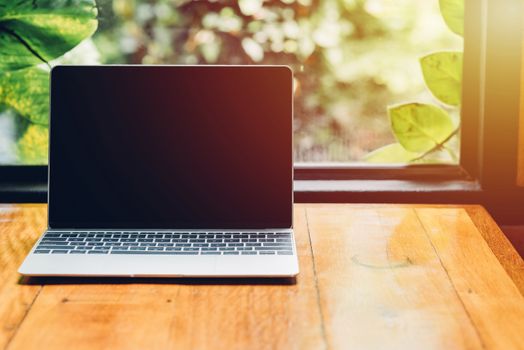 Laptop computer mockup with blank screen on desk in coffee shop.