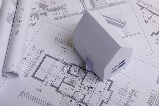 White family paper house, house projects plan and blueprints in the background. Minimalistic and simple concept, style. Horizontal orientation