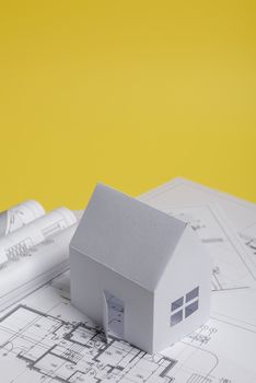 White family paper house, house projects plan and blueprints on yellow background paper. Minimalistic and simple concept, style. Vertical orientation.