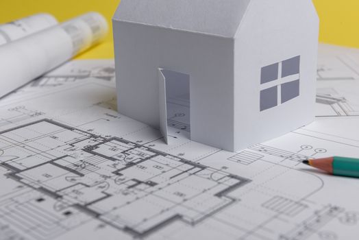 White family paper house, house projects plan and blueprints on yellow background paper. Minimalistic and simple concept, style. Horizontal orientation