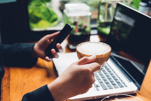 Young business woman is using his smart phone and The laptop computer in the cafe