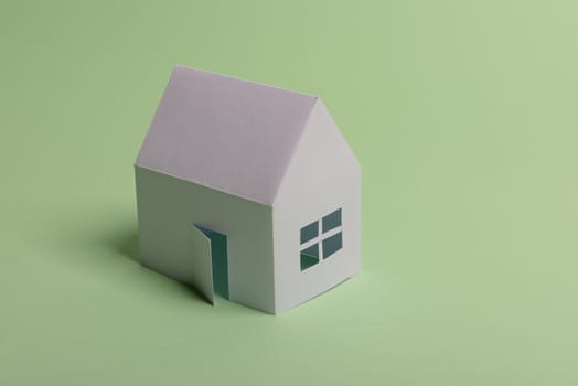 White family paper house in man hand on mint background paper. Minimalistic and simple concept, style. Copy space. Horizontal orientation