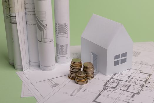 White family paper house , stack of money coins, house projects plan and blueprints on mint background paper. Minimalistic and simple concept, style. Horizontal orientation