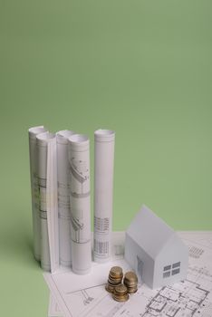 White family paper house , stack of money coins, house projects plan and blueprints on mint background paper. Minimalistic and simple concept, style. Vertical orientation