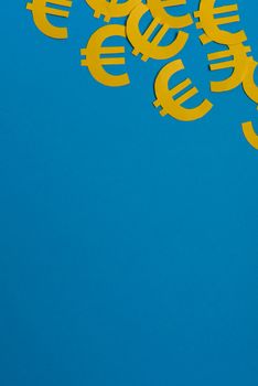 Paper yellow symbols of euro currency on blue background. View from above with copy space