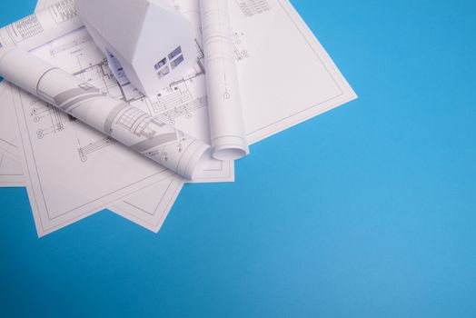 White family paper house, house projects plan and blueprints in the background. Minimalistic and simple concept, style. Horizontal orientation. View from above.