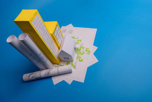 Paper skyscrapers , us dollar money, house projects plan and blueprints on blue background paper. Minimalistic and simple concept, style. Horizontal orientation. View from above. Copy space.