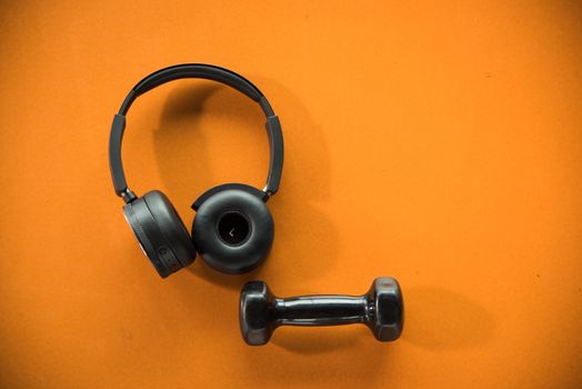 Music headphones and dumbbell on orange rubber floor in fitness gym