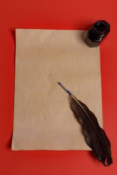 Raven feather, inkwell and old yellowed paper on red background. Copy space. Old letter.