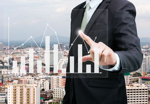 Businessman standing posture hand touch graph finance on City background