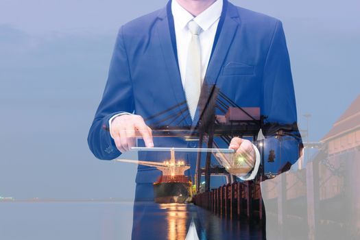 Double exposure of businessman hand hold tablet, cargo port ship at sea port concept