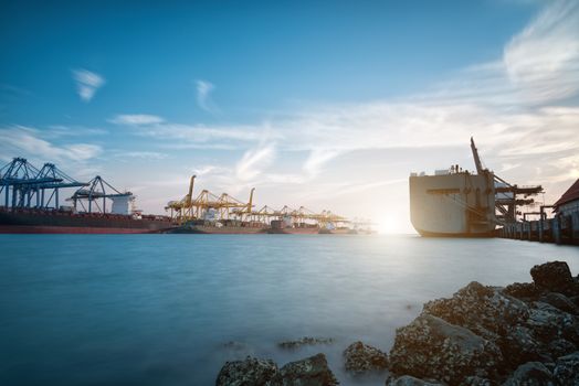 Cargo ship at Trade Port harbor with crane and blue sky over sea at sunrise