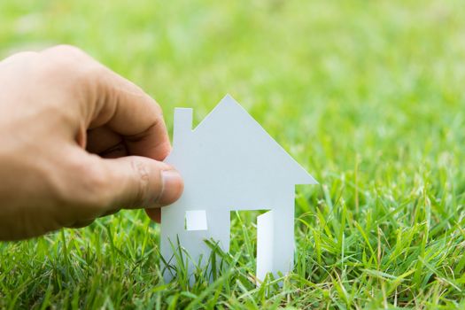 concept image of make house with white paper cut on green grass background