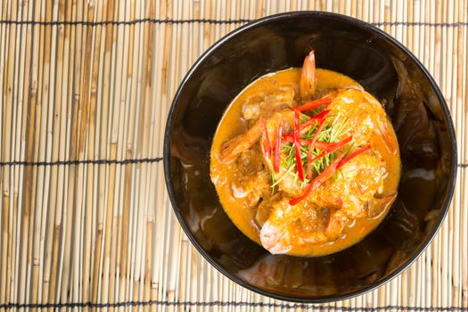Curry fried shrimps in black cup closeup on table with wooden background