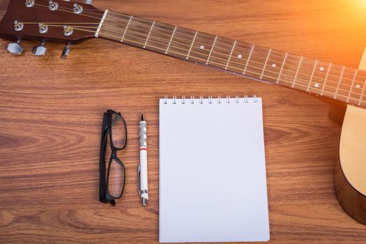guitar notebook, pencil and eyeglasses on wooden background