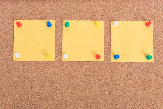 Yellow blank note papers with pin on wooden board background