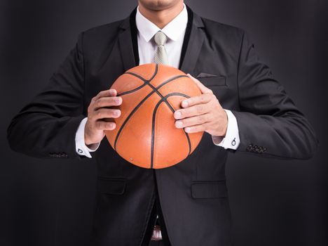 Young businessman holding basketball ball isolated on black background