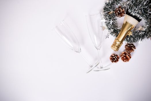 Christmas or New Year composition. Minimalistic concept of champagne bottle with two glasses, garland and pinecone decoration on white background. Christmas, winter concept. Flat lay, top view.