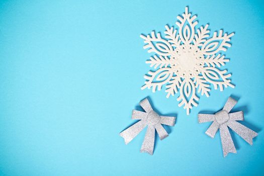 Christmas or winter composition. White snowflake with two glittery silver bows on pastel blue background. Christmas, winter, new year concept. Flat lay, top view, copy space.