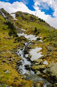 Mountain stream flows along the mountainside, snow. Nature background in spring or summer. Selective focus