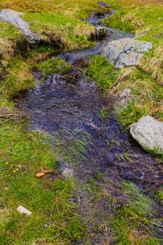 Mountain stream flows along the mountainside, snow. Nature background in spring or summer. Selective focus