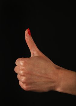 Woman hand with red nails showing thumb up, like, ok or good gesture isolated on black background, side view